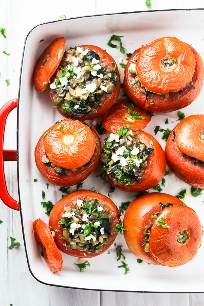 A top-view of vegetarian stuffed tomatoes in a white baking dish with red handles.