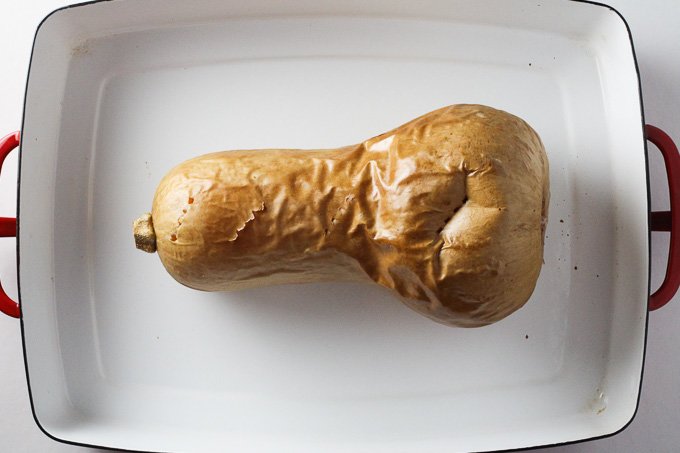 How to Cook Butternut Squash: Top view of a cooked whole butternut squash inside a white baking dish.