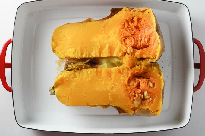 How to Cook Butternut Squash: A top view of a cooked butternut squash cut lengthwise inside a white baking dish.