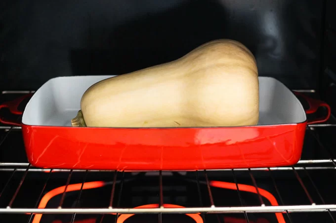 A butternut squash in a red baking dish inside an oven.