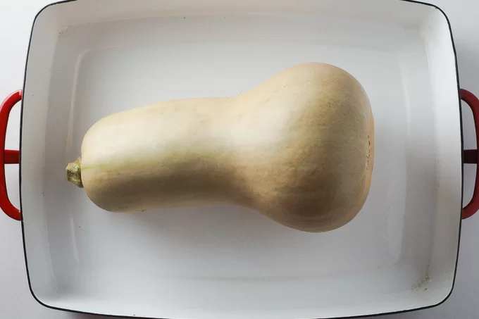 A top view of a butternut squash in a white baking dish.