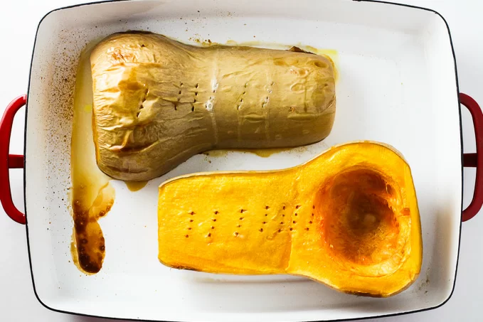 Top view of two cooked butternut squash halves inside a baking dish.