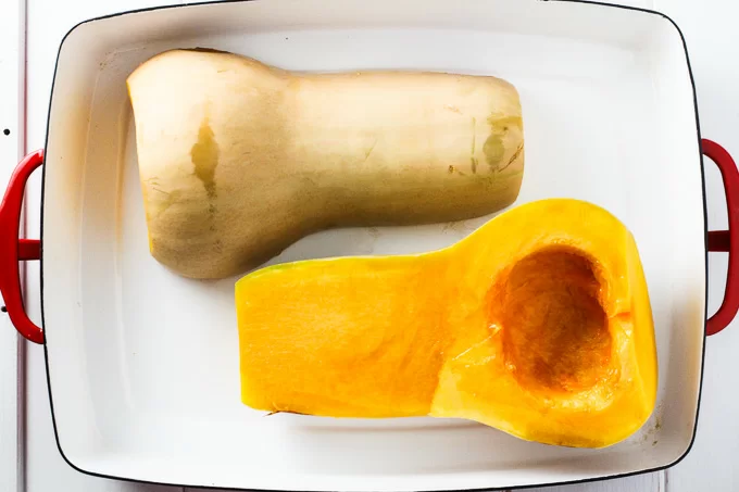 Top view of two butternut squash halves in a white baking dish.