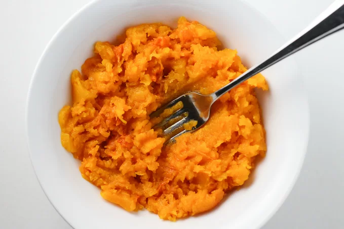 Butternut squash puree in a white dish with a fork in the middle.