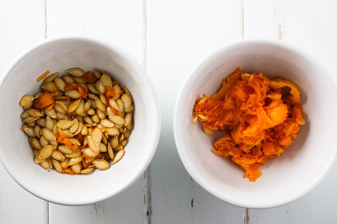 Top view of a white bowl with butternut squash seeds and a bowl with butternut squash pulp.