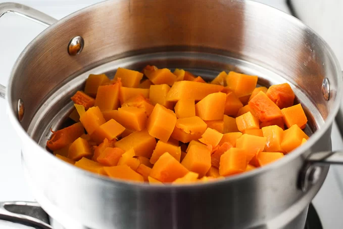 Close-up side view of cubed butternut squash being steamed in a steamer basket.