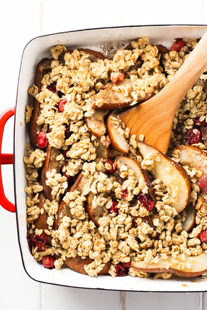 A close-up top view of a pear cranberry crisp with a wooden spatula in a baking dish. 