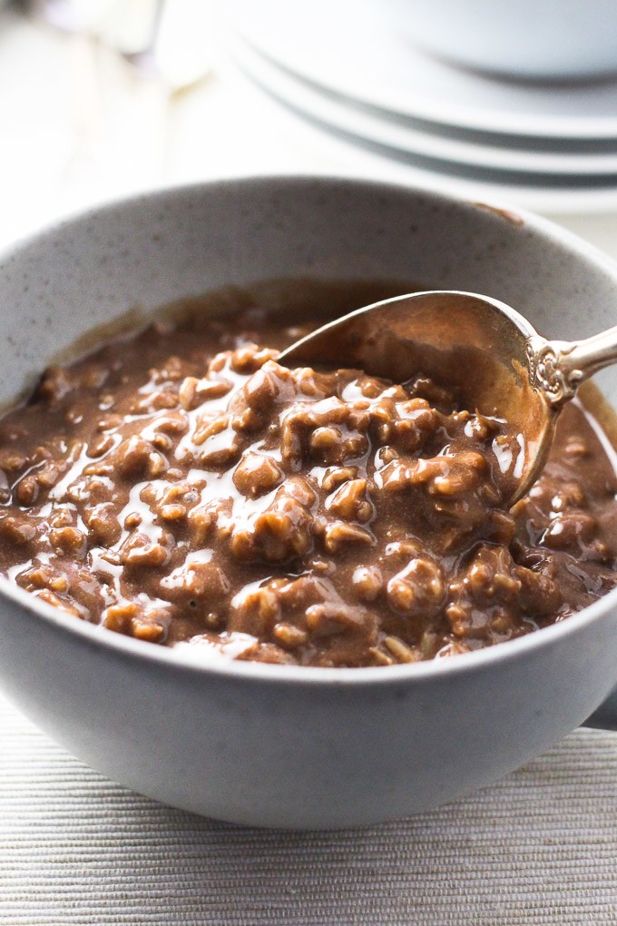 A close-up side view of the hot chocolate oatmeal in a grey bowl with a spoon in the oatmeal.