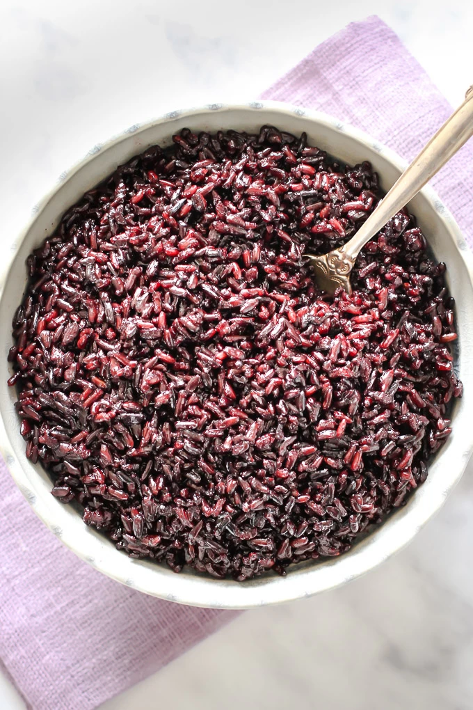 Cooked black rice in a round bowl standing on a purple napkin.