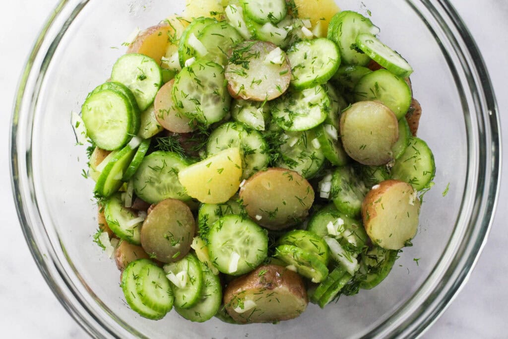 Tossed potato cucumber salad with fresh dill and vinegar dressing in a bowl.