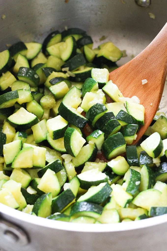 Sauteed zucchini in a pan being stirred with a wooden spoon.