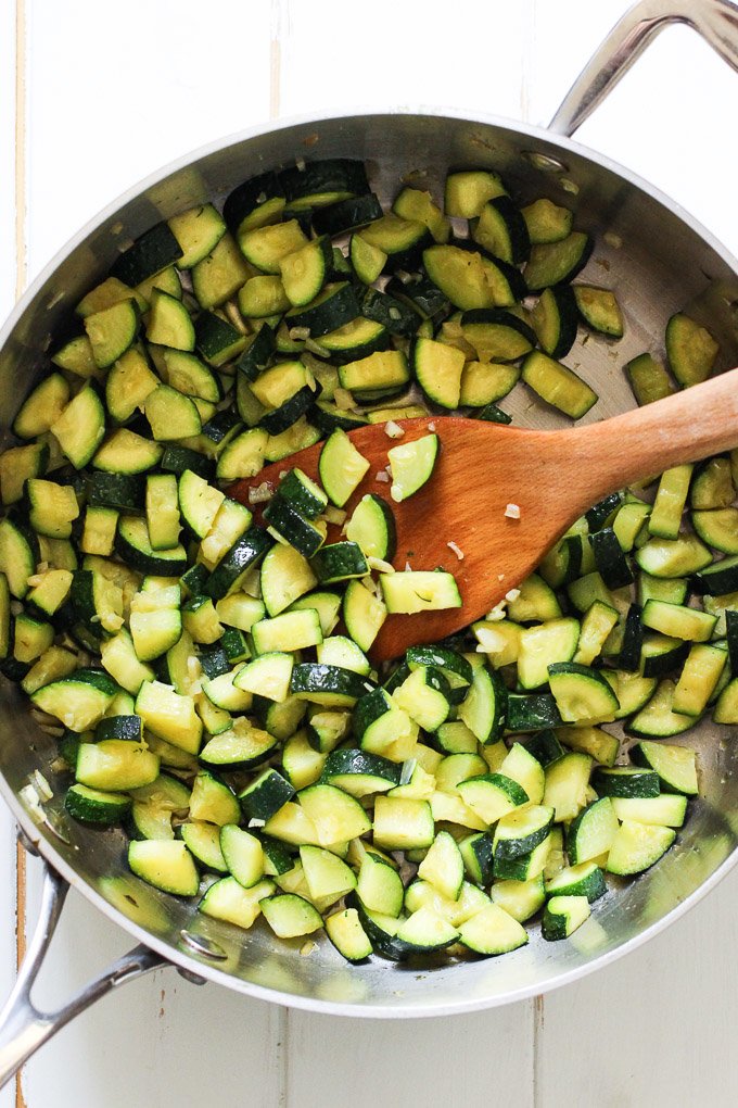 Sauteed zucchini in a pan with a wooden spoon in the middle.