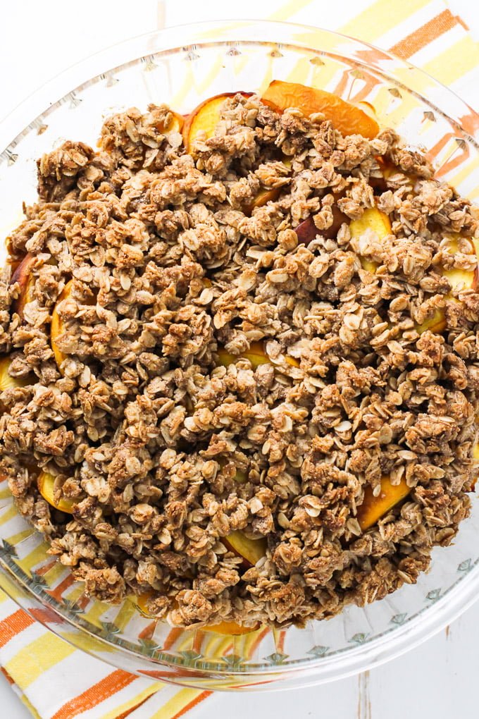 Healthy peach crisp in a round glass baking dish standing on a tea towel.