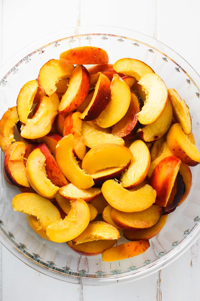Peach slices in a glass baking dish standing on a white background.