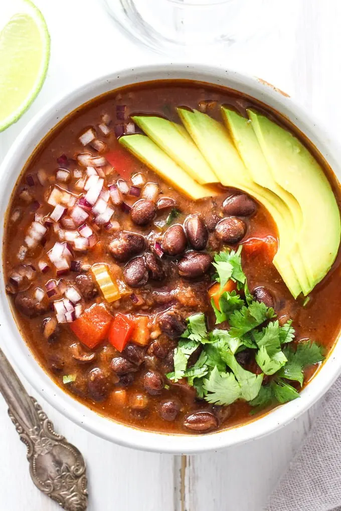 A bowl of black beans soup garnished with avocado, onion, and cilantro. Top view.