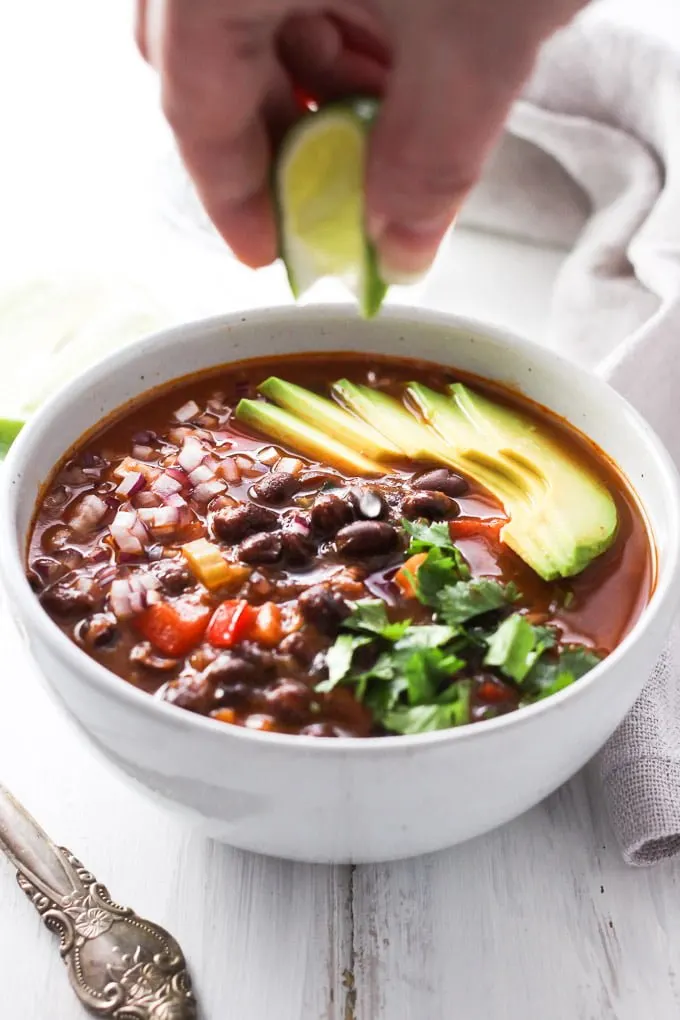 A bowl of canned black bean soup garnished with avocado, onion, fresh cilantro and lime juice.