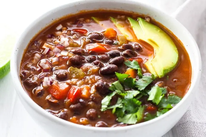 A bowl of black beans soup garnished with avocado, cilantro, and onion. Side view.