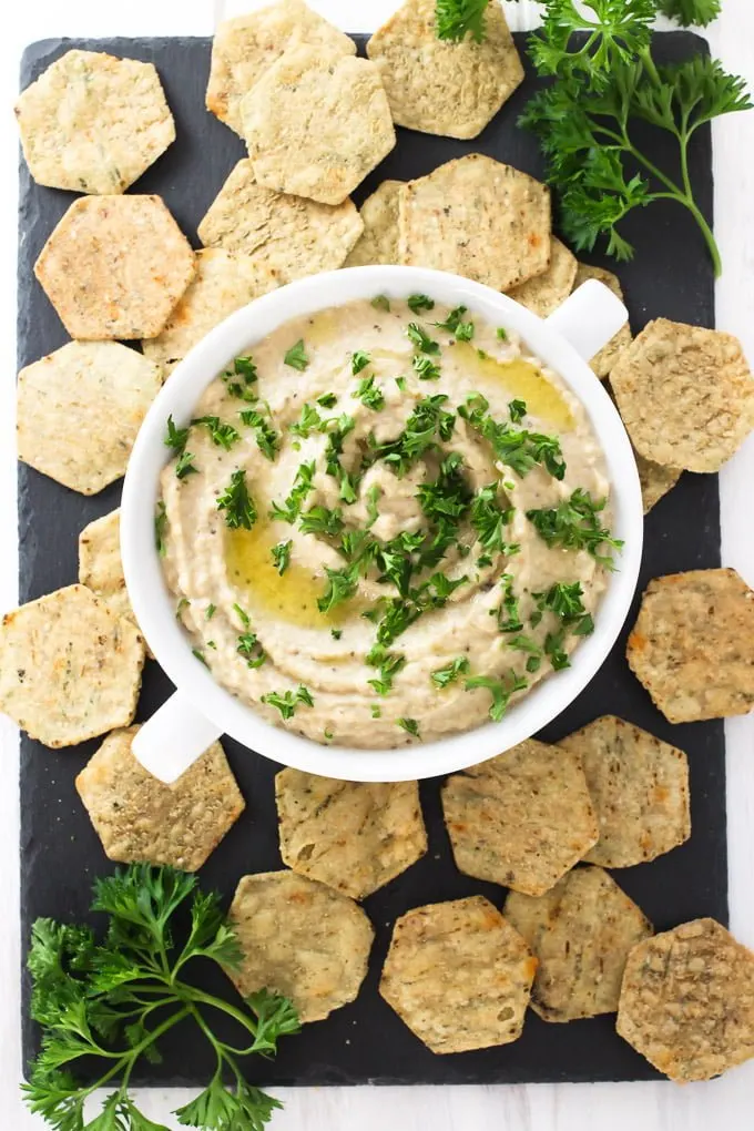 Creamy baba ganoush in a bowl, garnished with chopped parsley. Served with crackers.