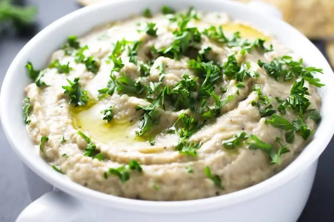 Baba ganoush in a white bowl, garnished with chopped parsley and olive oil.