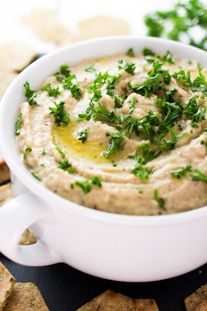 Creamy baba ganoush in a white bowl, garnished with chopped parsley.