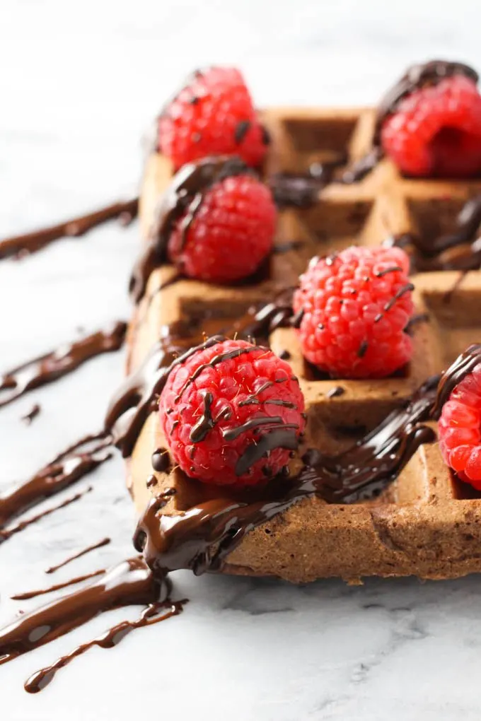 Chocolate waffle topped with fresh raspberries and chocolate sauce. Side view.