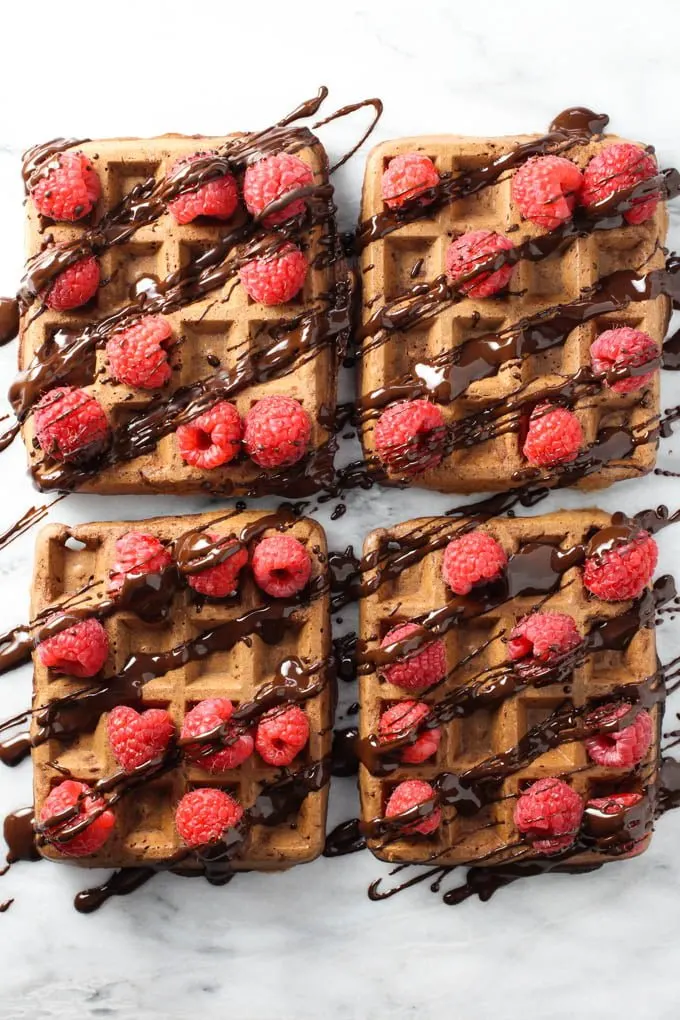 Four healthy chocolate waffles topped with fresh raspberries and chocolate sauce. Top view.