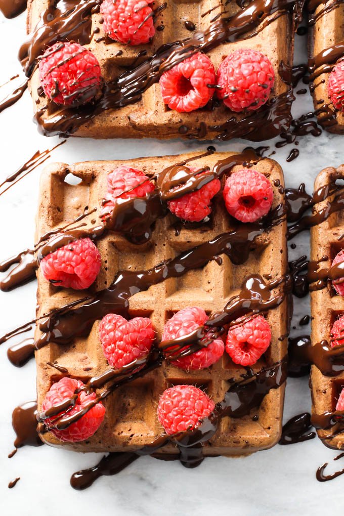 Close up of a chocolate waffle topped with fresh raspberries and chocolate sauce. Top view.