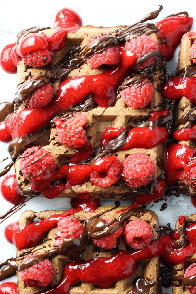 Close up of a chocolate waffle topped with fresh raspberries, chocolate sauce, and raspberry sauce. Top view.