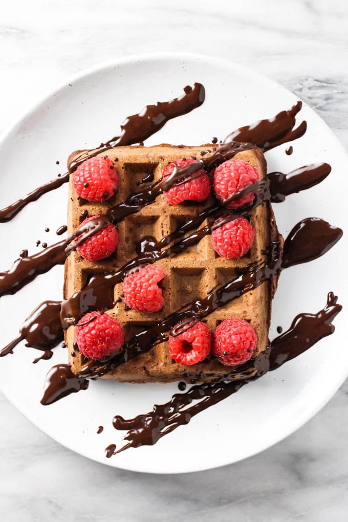 Healthy chocolate waffle topped with raspberries and chocolate sauce on a white plate. Top view.