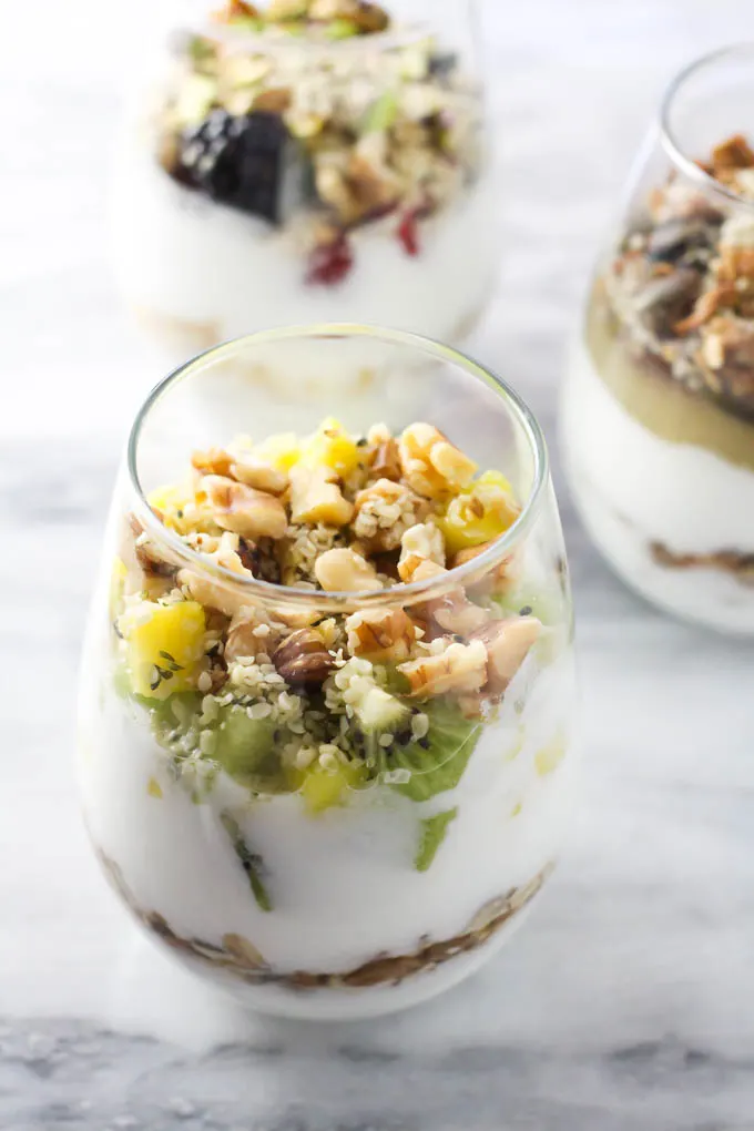 Fruit and nut yogurt parfait in a glass on a marble background.