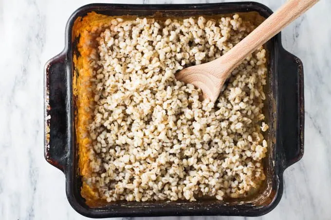 Oven-baked pot barley in a baking dish with a wooden spoon.