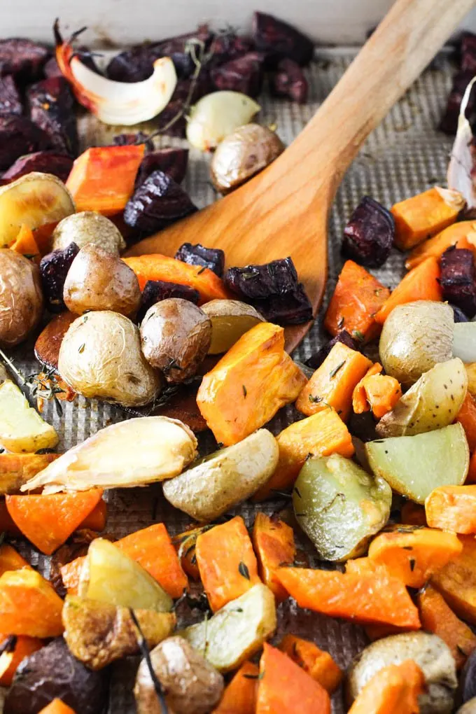 Roasted root vegetables on a baking sheet with a wooden spatula.