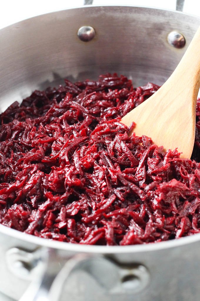 Sauteed beets in a pan with a wooden turner.