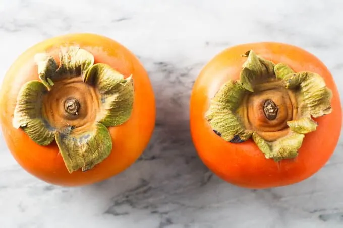 Two Fuyu persimmons on marble background.