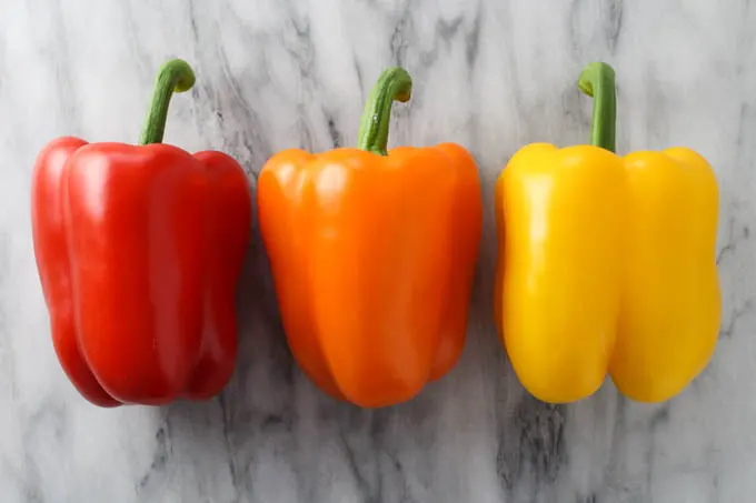 Three fresh bell peppers - red, orange, and yellow.