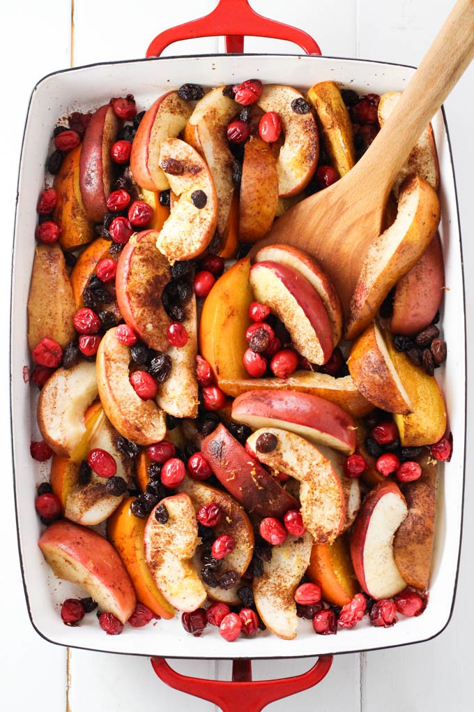 Overhead shot of mixed baked fruit in a baking dish. A wooden spatula is in the fruit.