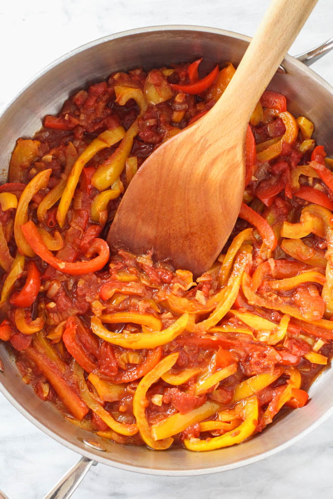 Peperonata in a skillet with a wooden spatula in it.