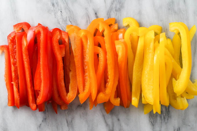 Red, orange, and yellow bell peppers sliced into thin strips.