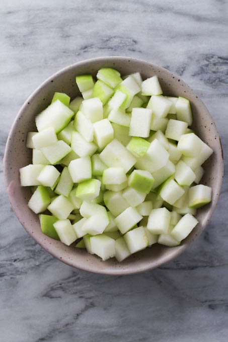 Diced green apple in a bowl on marble background.