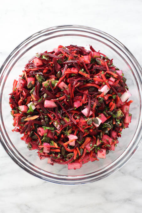 Raw beet salad in a glass salad bowl on marble background.