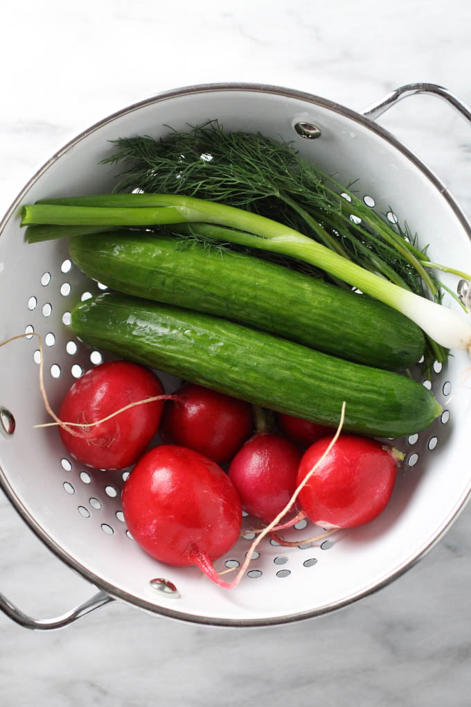 Washed radishes, cucumbers, green onions, and dill in a colander.