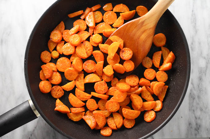 Sautéed carrots in a skillet being mixed with a wooden spoon.