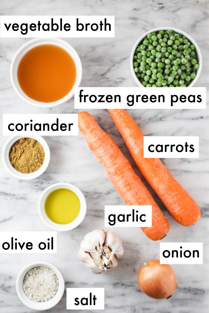 The ingredients for peas and carrots recipe displayed on marble background. The ingredients are labeled as follows: vegetable broth, frozen green peas, coriander, carrots, garlic, olive oil, salt, onion.