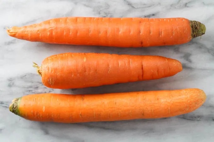 Three raw unpeeled carrots on a marble background.