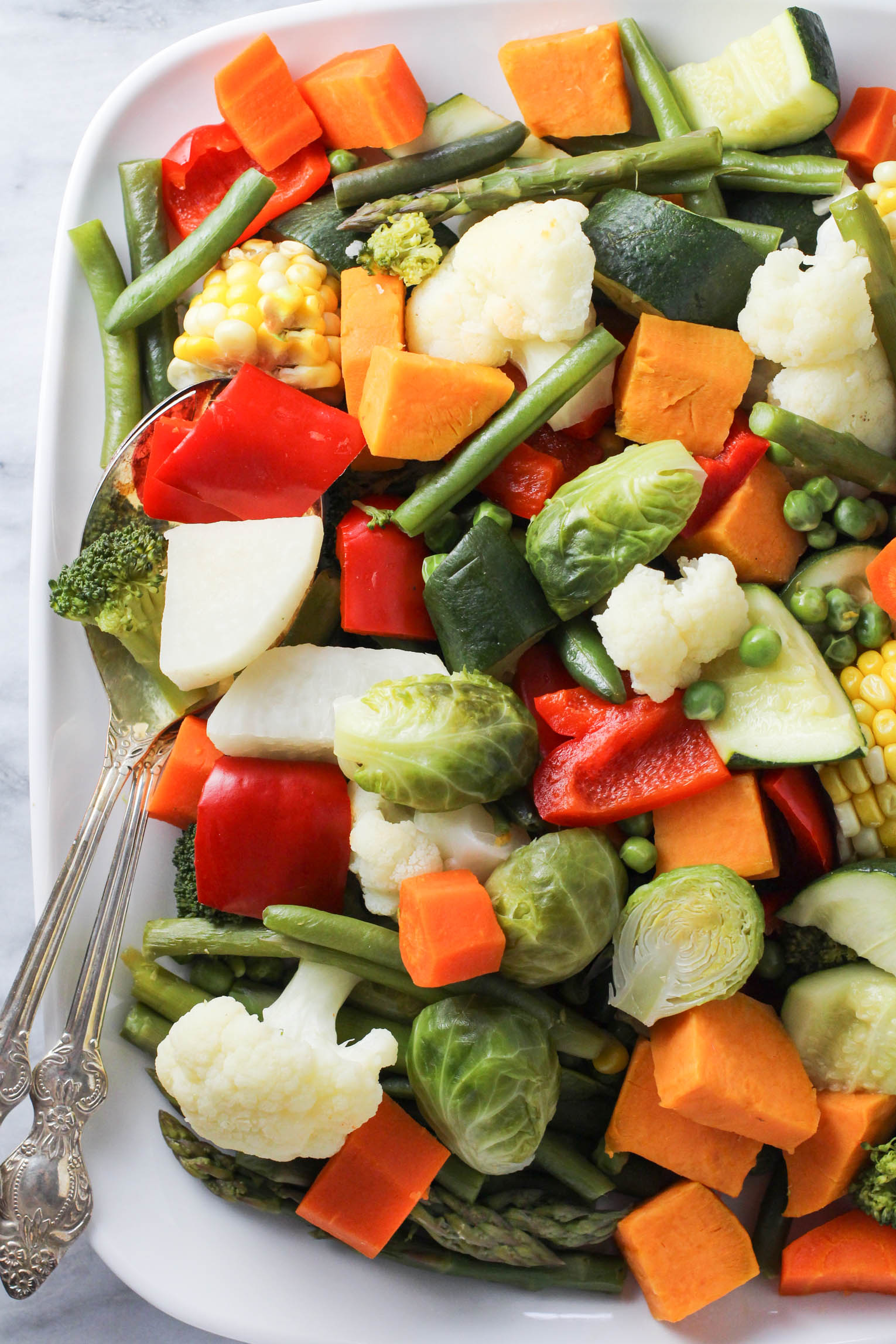 Instant Pot steamed vegetables on a white platter. Two silver serving spoons on the left side.