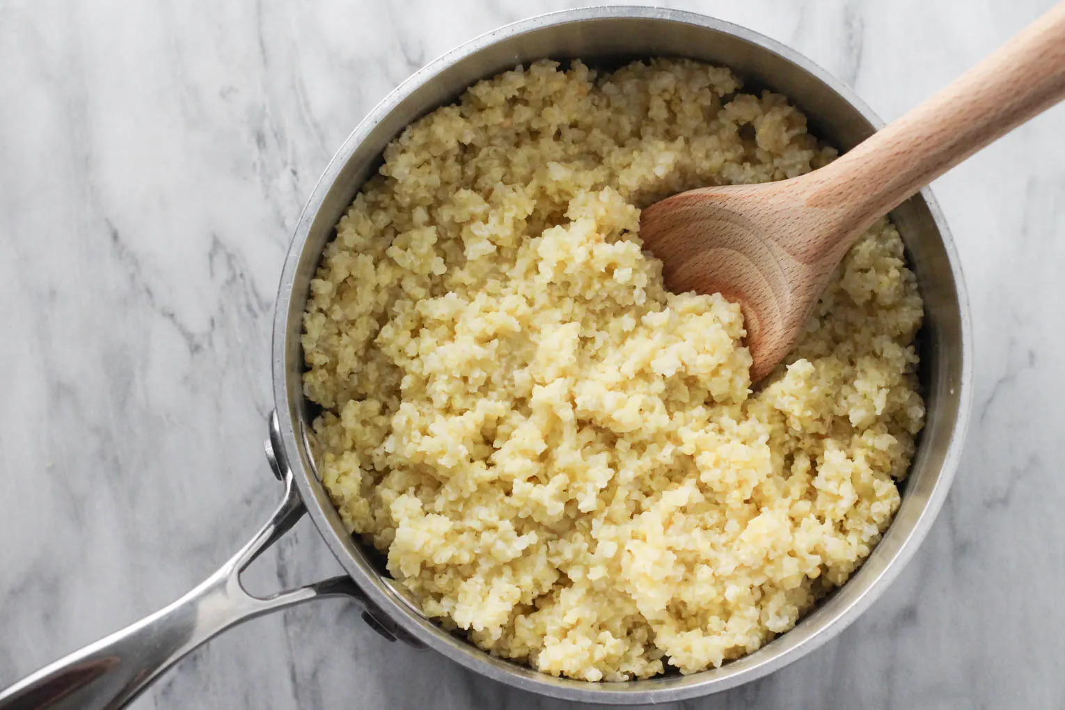 Cooked millet in a pot with a wooden spoon in the millet.