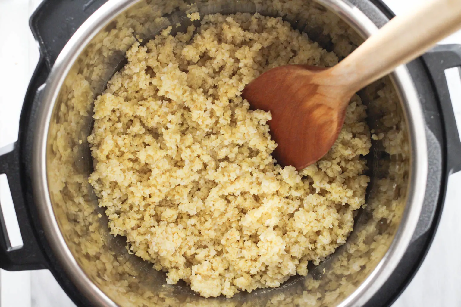 Cooked millet inside an Instant Pot with a wooden spatula in the millet.