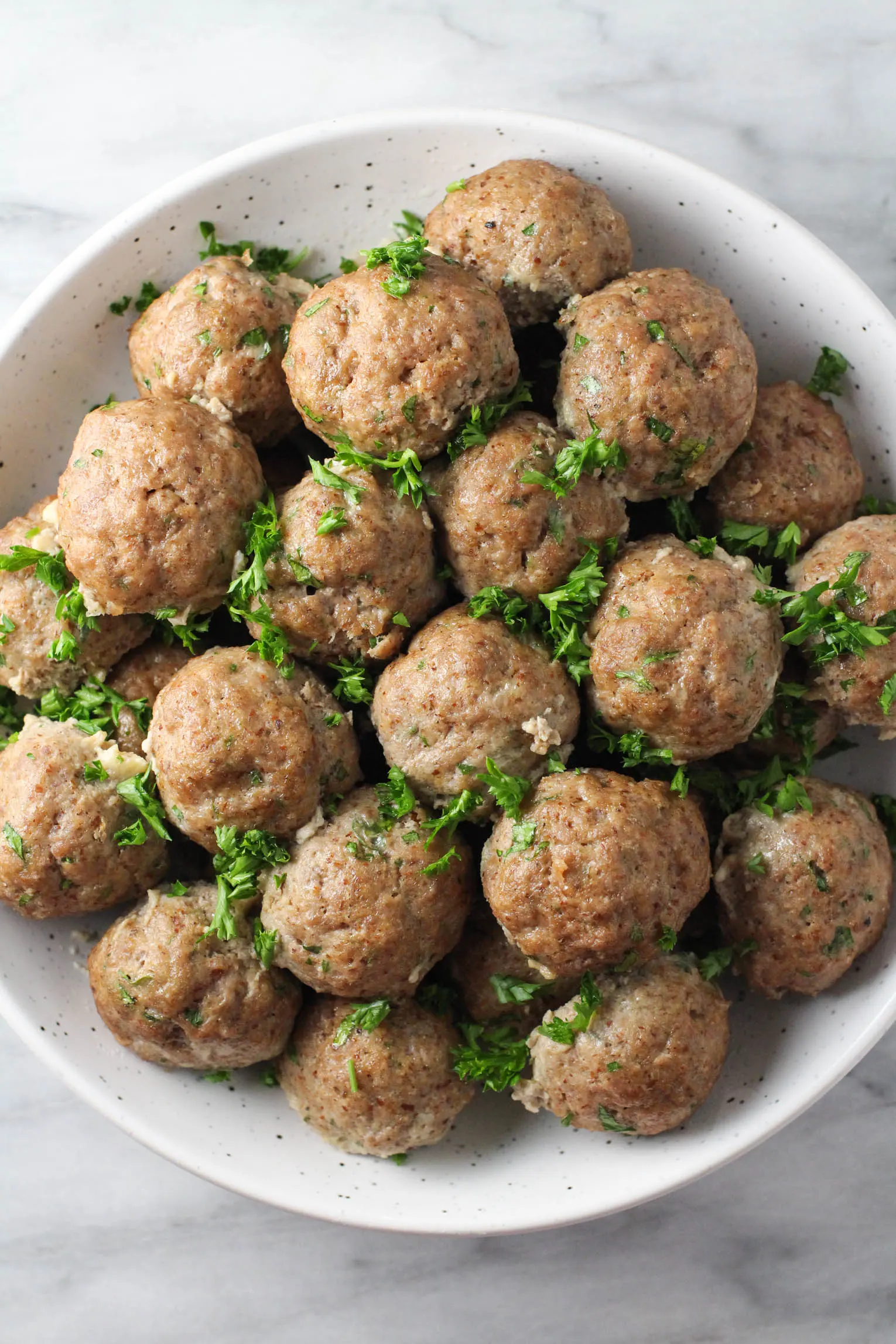 Overhead shot of meatballs without breadcrumbs in a bowl. The meatballs are garnished with parsley.