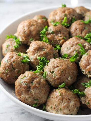 Meatballs without breadcrumbs in a white bowl garnished with chopped parsley.