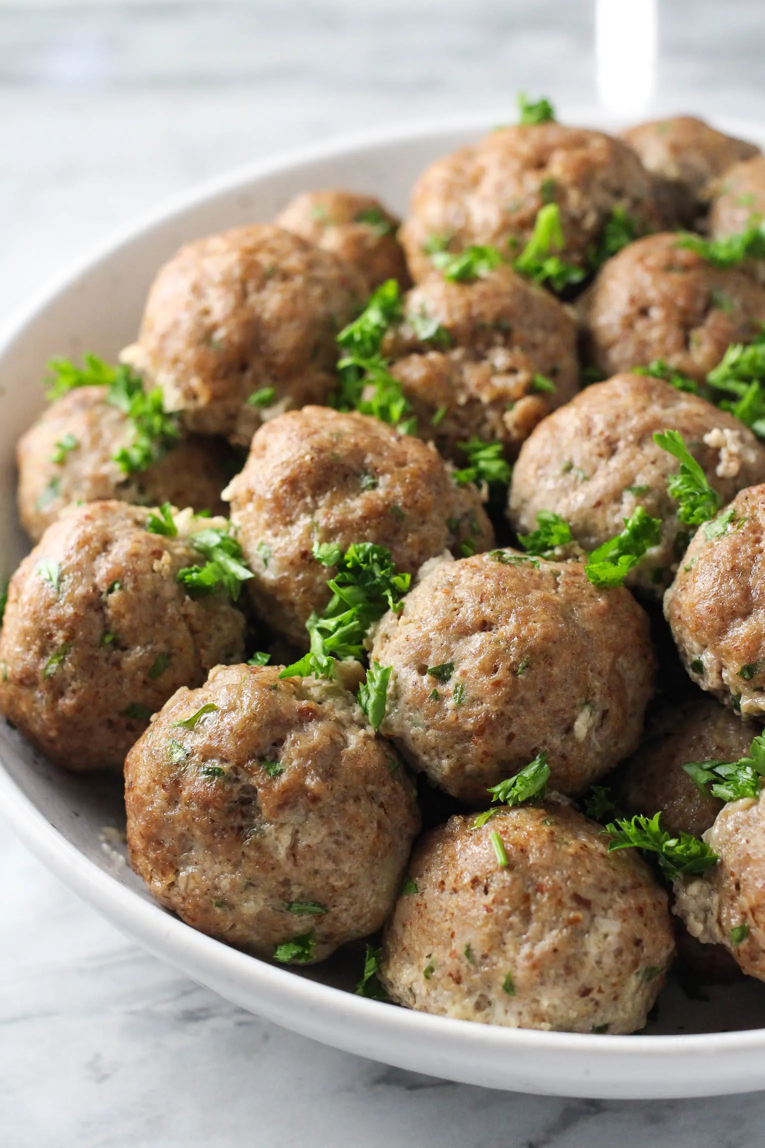 Meatballs without breadcrumbs in a white bowl garnished with chopped parsley.